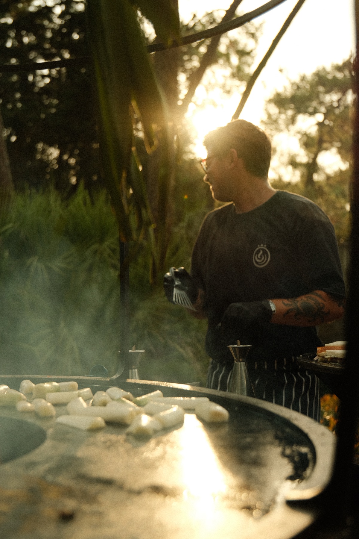 Le chef de Maison Gomary au brasero, à contre-jour, dans la lumière d'un coucher de soleil